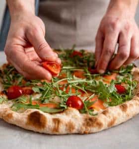 close up man putting tomatoes baked pizza dough with smoked salmon slices 2